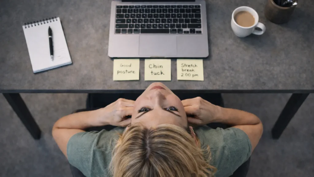 Mulher no escritório com lembretes de postura correta para exercícios de jawline, demonstrando a rotina diária de chin tuck e alongamentos cervicais no ambiente de trabalho para prevenir a síndrome da cara quadrada causada pelo uso do celular e computador